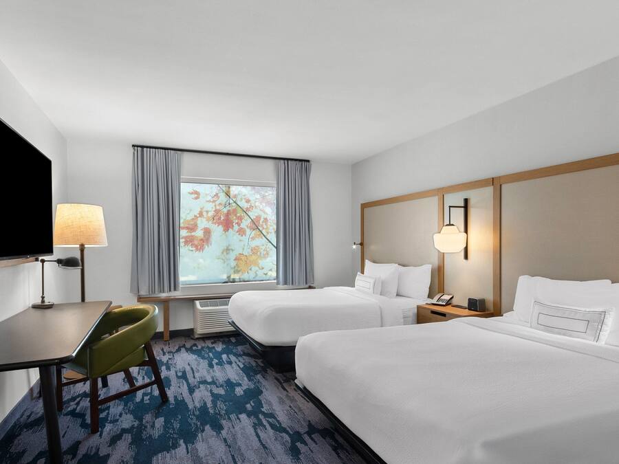 A hotel room with two beds, a desk, a chair, a TV, and a window with curtains.