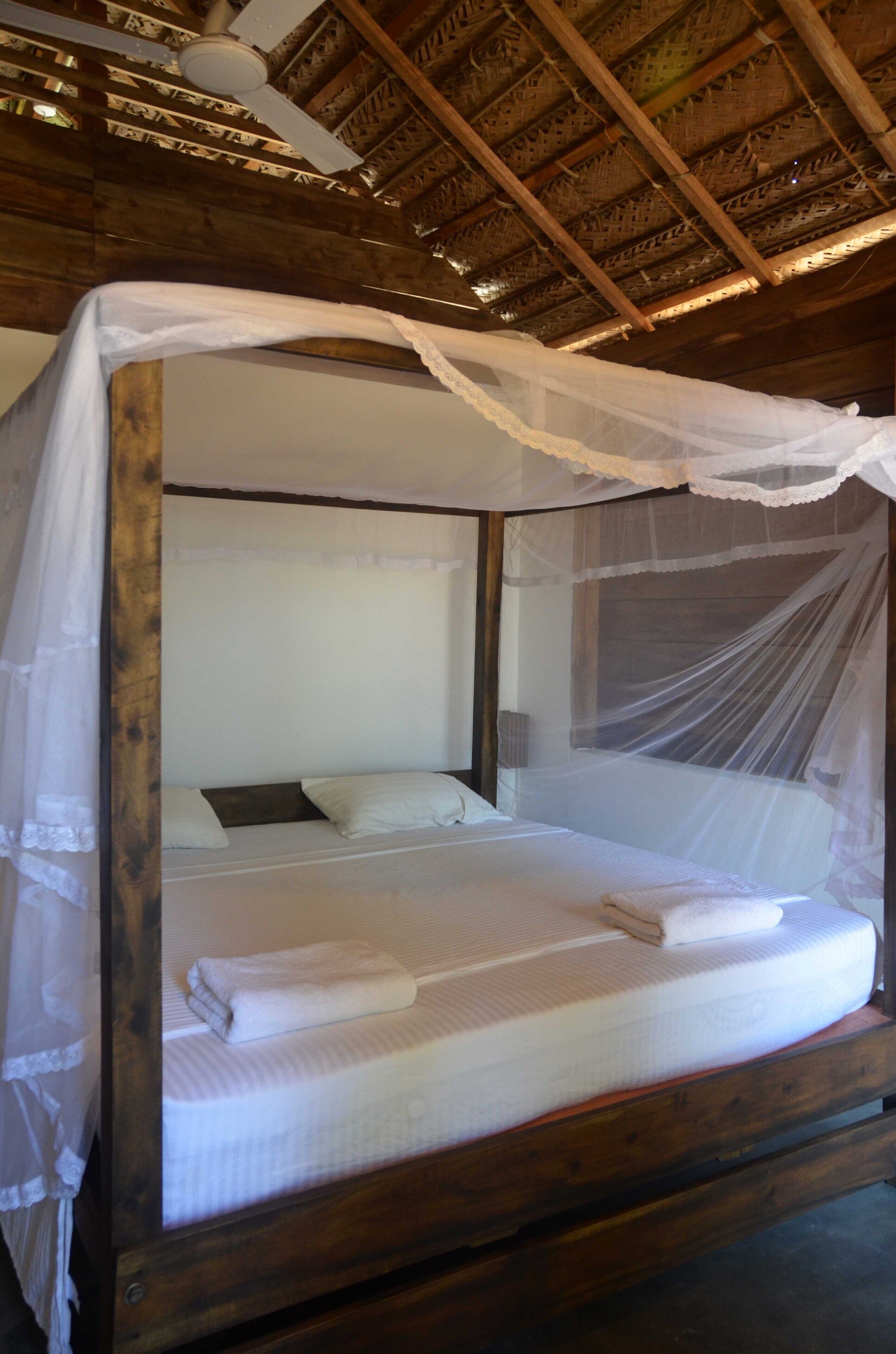 A bed with a canopy, wooden headboard, and a white mattress.