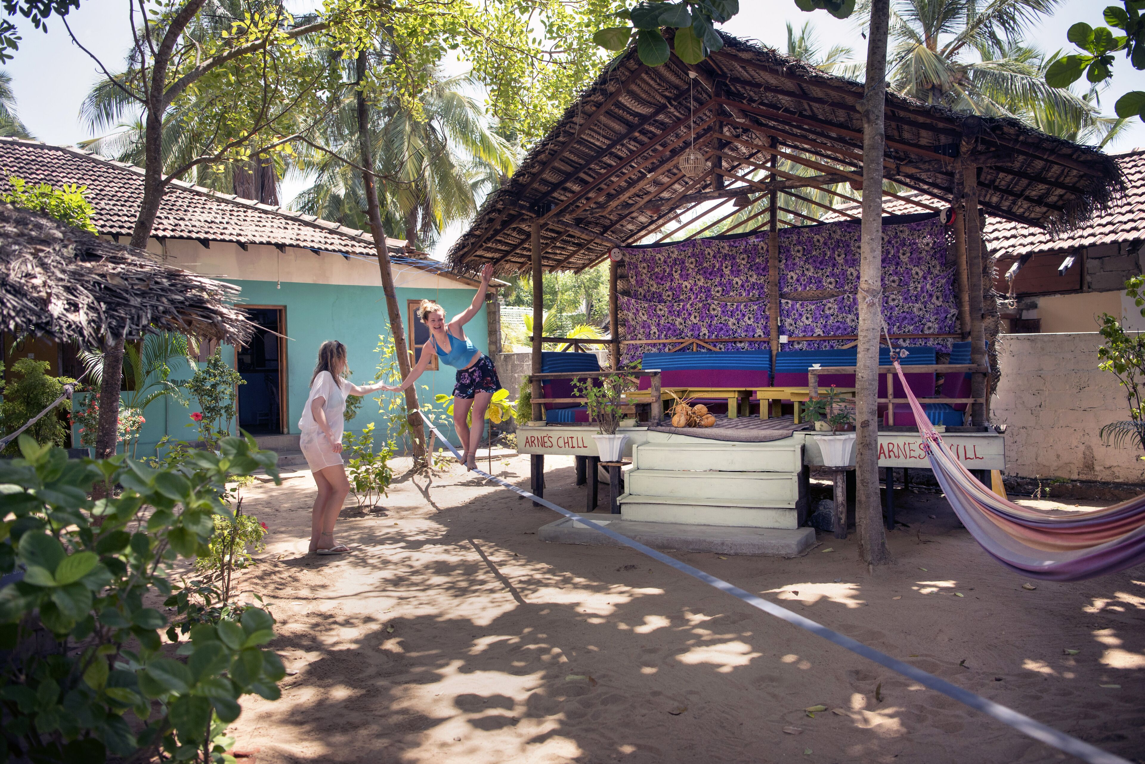 Un espacio al aire libre rústico con una hamaca, una zona de estar cubierta con estampado floral púrpura, y un letrero que dice "ARNES CHILL".