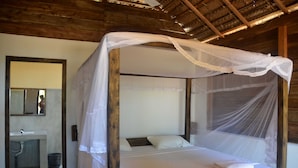 Un lit à baldaquin, un plafond en bois et une salle de bain équipée d’un lavabo et d’un miroir.