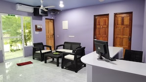 A reception area with a white desk, two black wicker chairs, a small table with a green bowl, and two wooden doors. - Hudhu Velaa (Dhonfanu)
