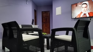 A room with two black wicker chairs with white cushions, a small table, and a television mounted on the wall. - Hudhu Velaa (Dhonfanu)