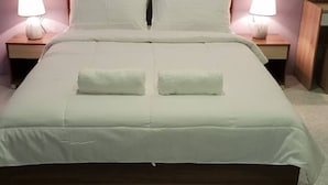 A neatly made bed with two pillows, a wooden nightstand with a lamp, and a small stool. - Hudhu Velaa (Dhonfanu)