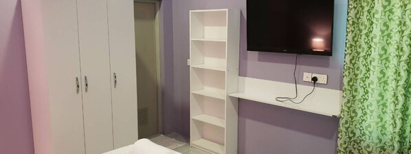Un dormitorio con un armario, un televisor montado en la pared y una cortina estampada.