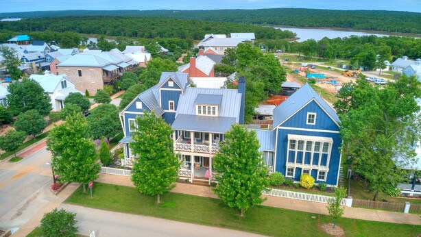 A large blue house with a porch, surrounded by trees and a lake in the background. - Carlton Landing-Spacious home on Boulevard (Eufaula)