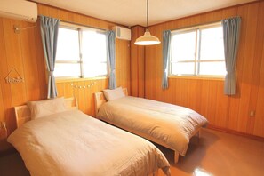 Une chambre avec deux lits simples, des murs en bois, un luminaire suspendu et une fenêtre avec des rideaux.