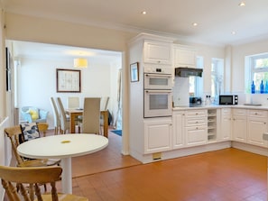 A modern kitchen with white cabinetry, a dining area with a round table, and a view of the outdoors through a window. - Bay House, Aldwick Bay  - sleeps 7 guests  in 4 bedrooms (Bognor Regis)