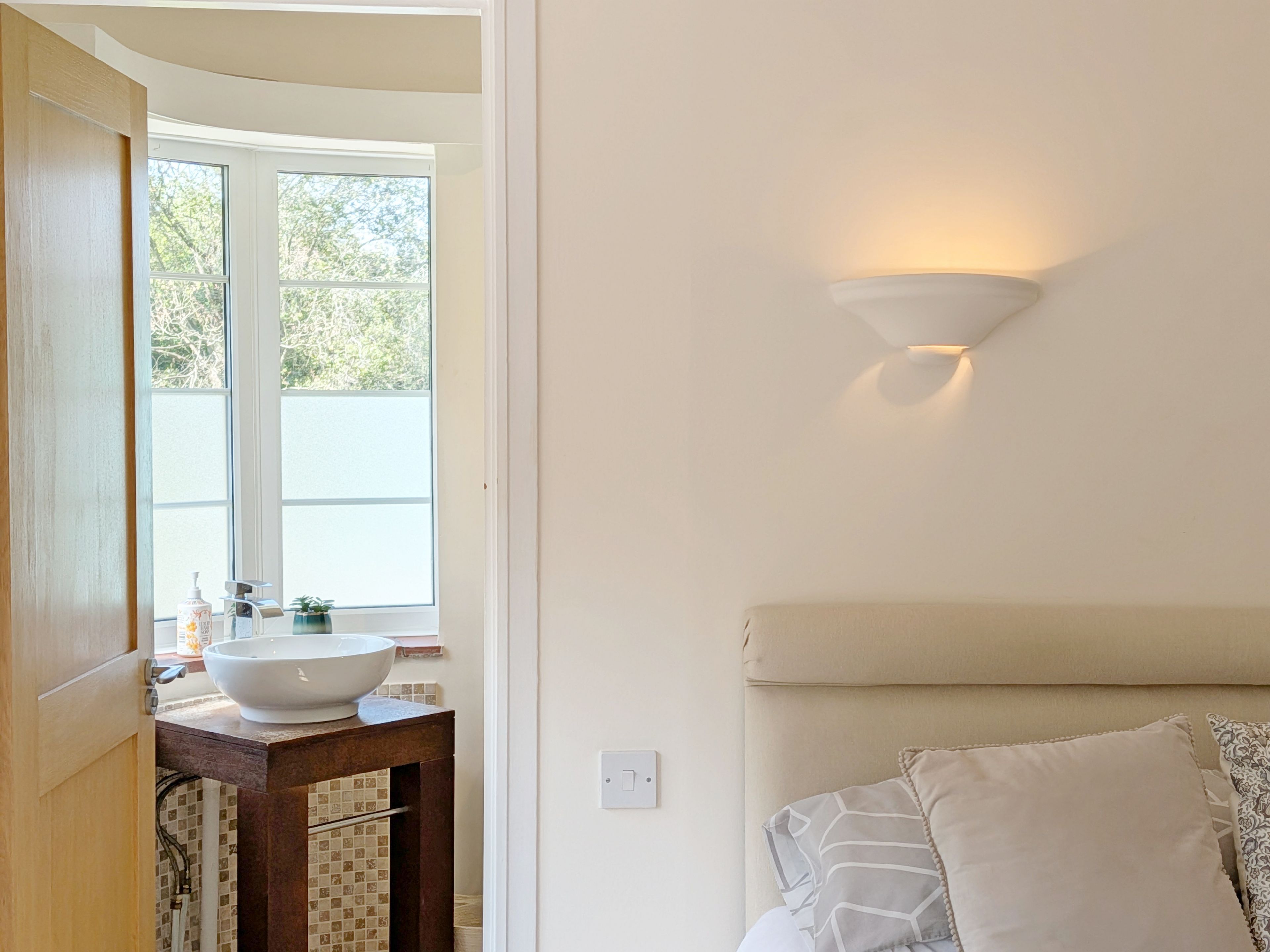 A bathroom with a white sink, a window, and a wall-mounted light fixture.