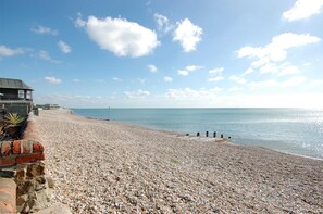 Une plage de galets avec un bâtiment sur la gauche, un ciel dégagé et une eau calme.