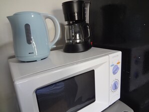 En mikrobølgeovn med elkedel og kaffemaskine ovenpå.