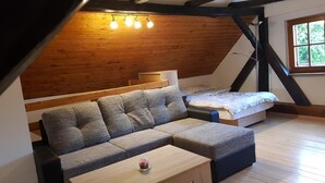 A loft bedroom with a wooden ceiling, a sofa, a bed, and a small table. - Vacation House Donacka Gora (Rogatec)