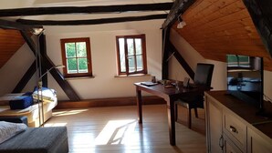 A room with a sloped ceiling, wooden beams, a bed, a desk with a chair, a television, and two windows. - Vacation House Donacka Gora (Rogatec)