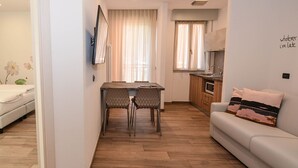 A compact living space with a bed, a dining area with two chairs, a kitchenette, and a sofa. - Albergo Pieve (Ledro)