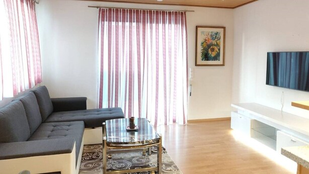 Ett modernt vardagsrum med en grå hörnsoffa, ett soffbord i glas och en platt-TV placerad på ett vitt TV-bord.