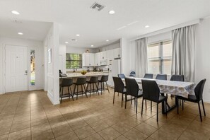 A modern kitchen with white cabinets, a dining area with a table and chairs, and a view of the outside through large windows. - EV_2609 - 4 Bed 3 Bath Villa with Screened-in Pool and Access to Resort Amenity (Davenport)