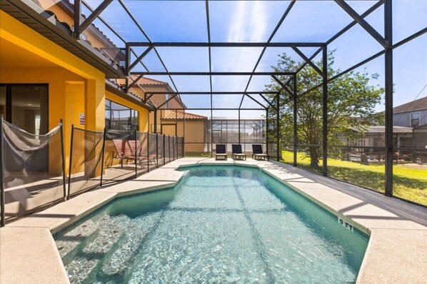 A swimming pool with a glass enclosure, sun loungers, and a yellow building.