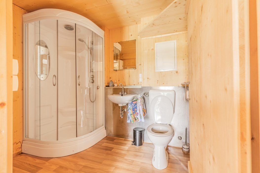 Une salle de bain rustique, aménagée dans une cabane en bois, comprenant une douche, un lavabo, des toilettes et un miroir.