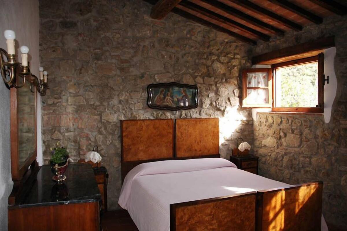 Un dormitorio con pared de piedra, cama de madera, mesita de noche, cómoda y ventana con vistas.