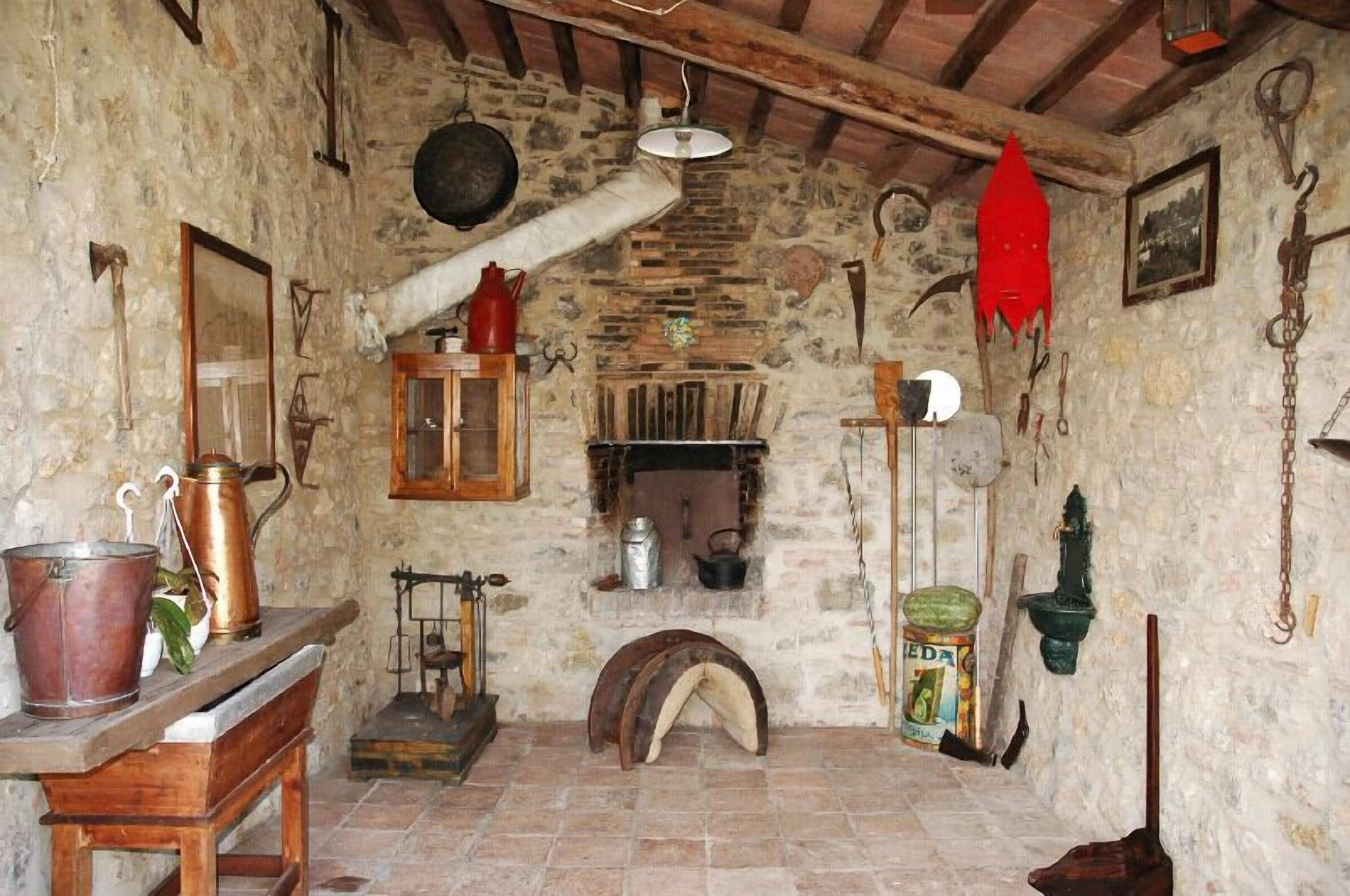 A rustic stone-walled room with a wooden bench, a hanging pot, a wooden cabinet, and a stone fireplace.