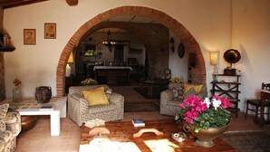 Un soggiorno rustico con un arco in pietra che conduce a una cucina, con arredi in legno e un vaso grande pieno di fiori.