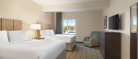 A hotel room with two beds, a desk, a chair, a television, and a view of the outdoors.