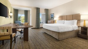Quarto de hotel com cama, escrivaninha, cadeira e televisão.
