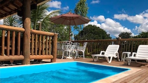 Une terrasse en bois avec une piscine, des chaises longues blanches et une table avec des chaises.