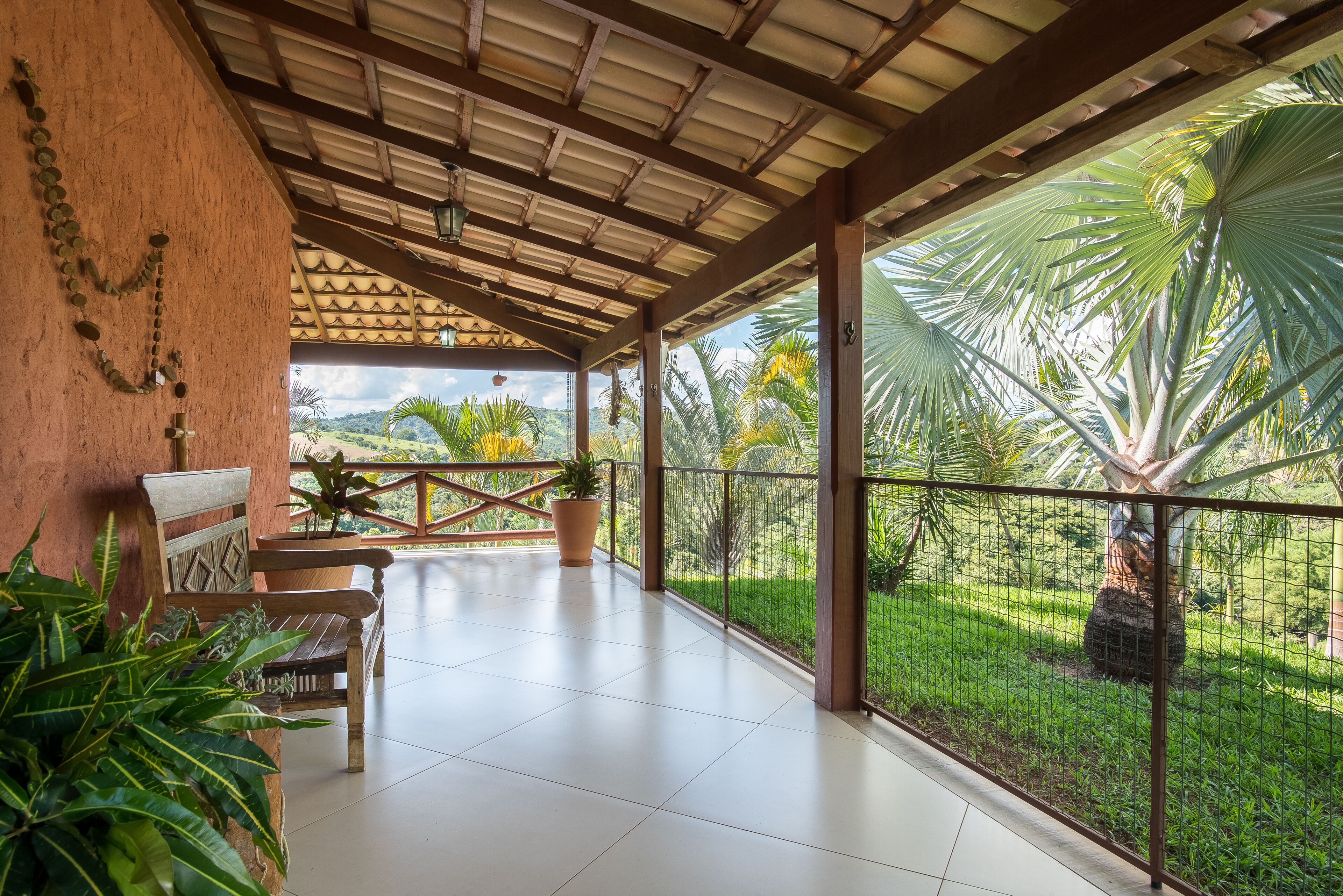 A covered patio with a wooden bench, potted plants, and a view of a lush garden.