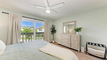 A bedroom with a bed, a dresser, a mirror, a ceiling fan, and a balcony with curtains.