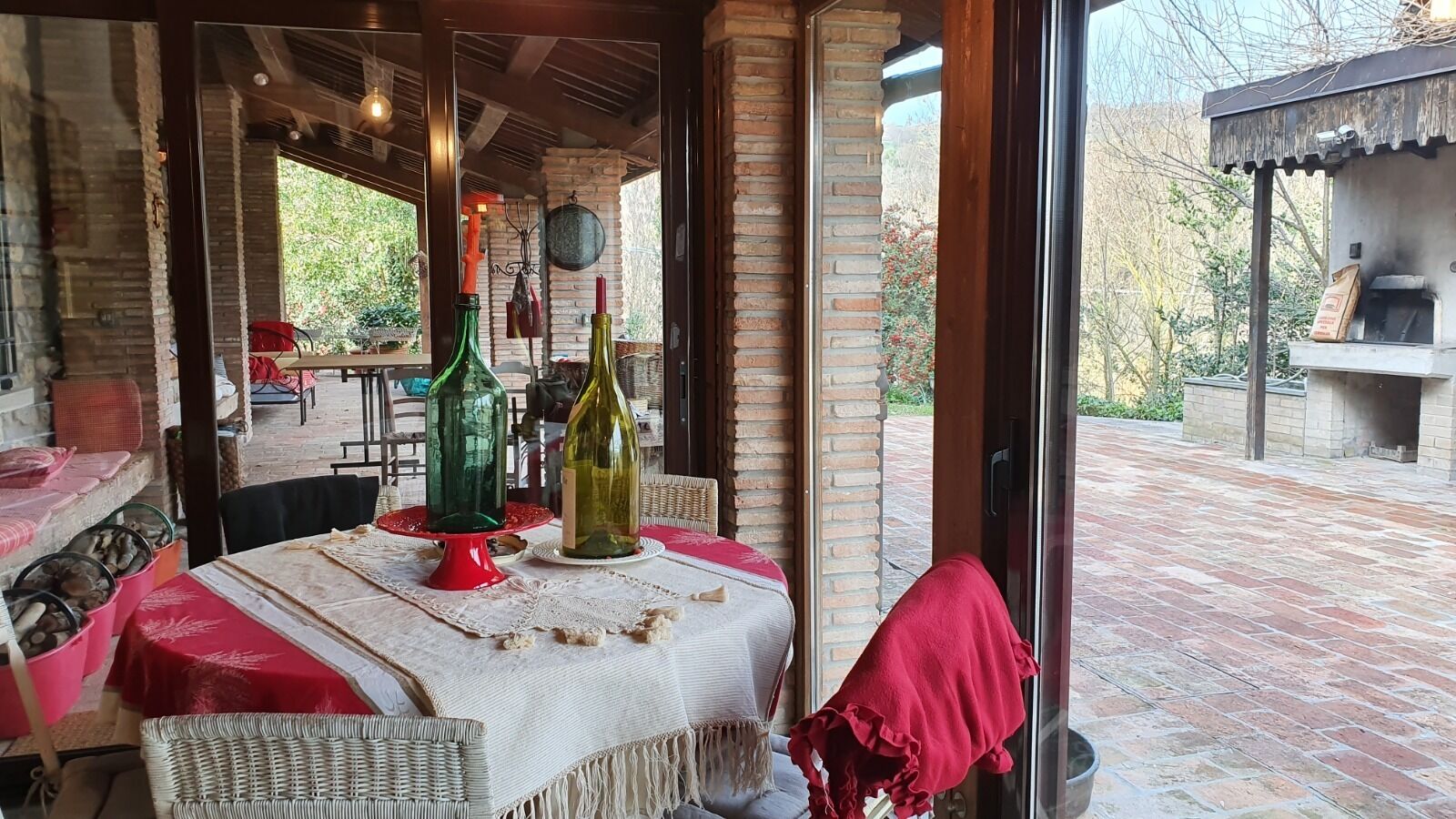 An outdoor dining area with brick flooring, wicker chairs, and tables set with red tablecloths.