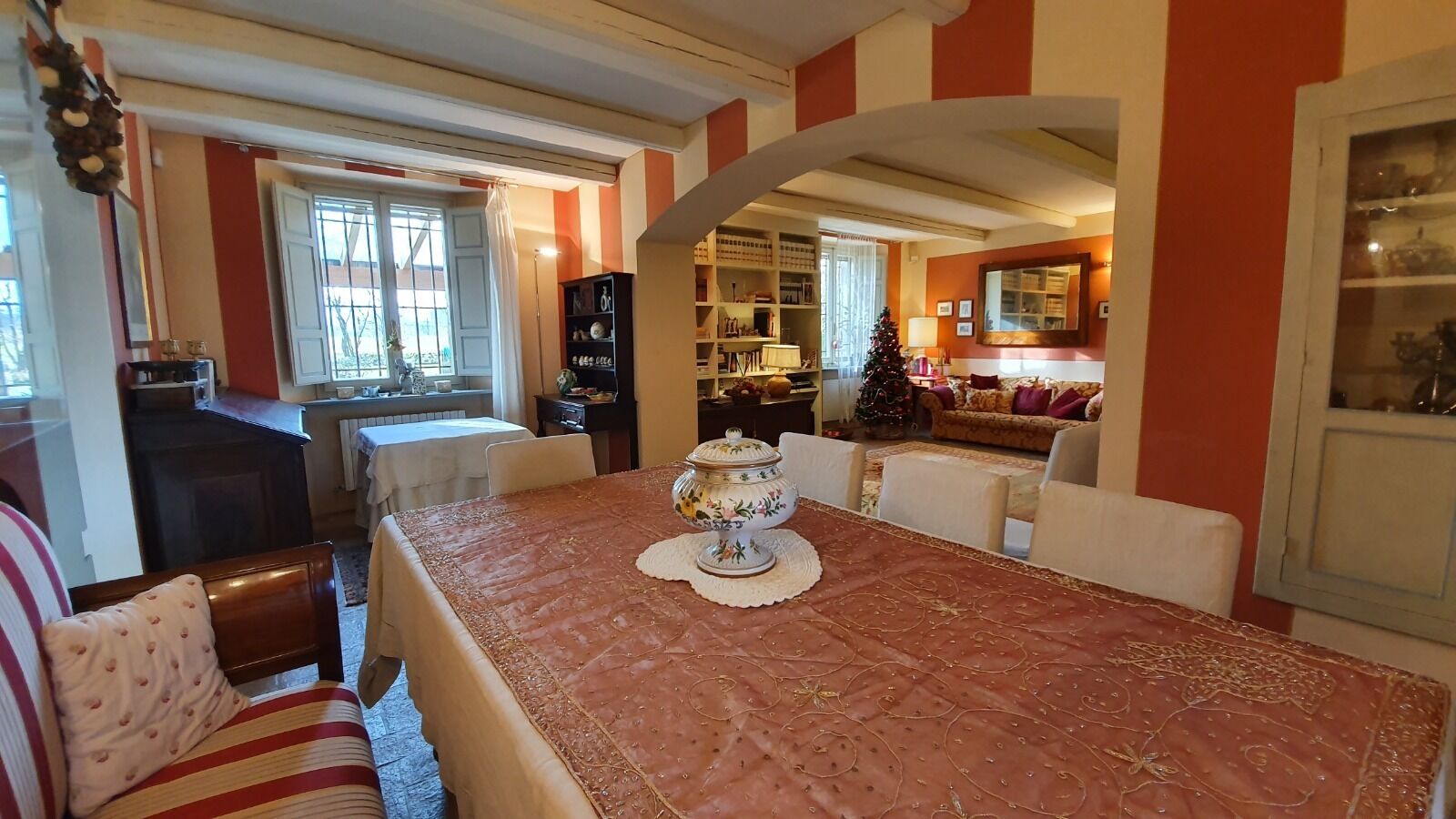 Un coin repas avec une table dressée pour quatre personnes, un sapin de Noël et une cuisine en arrière-plan.