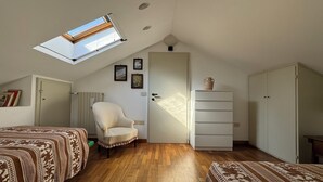 Una stanza con soffitto a falde, un lucernario, una sedia, una cassettiera e due letti.