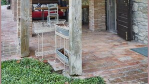 Un'area esterna coperta con pareti in pietra e travi in legno, con una panca in metallo e una sedia rossa.