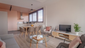 A modern living room with a glass coffee table, a sofa, a TV, and a dining area with chairs and a table. - ✨Mountain Suite ✨ stylish apartment with WiFi and Parking 🅿️ (Seynod)