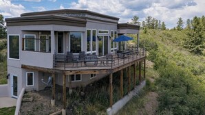 Une maison moderne à deux étages, dotée d’un balcon, de grandes fenêtres et d’un espace salon extérieur.