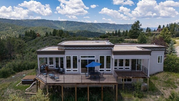 Une maison moderne dotée d’une terrasse, de grandes fenêtres et offrant une vue sur le paysage environnant.