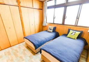 Une chambre avec deux lits, des murs en bois, une fenêtre avec des rideaux et un sol à motifs.