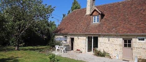 A stone house with a tiled roof, a chimney, and a small porch with outdoor seating.