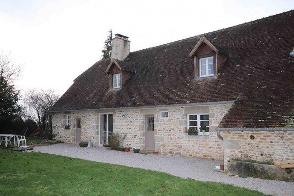 A stone house with a sloped roof, a chimney, and a small porch area.