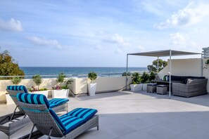 A rooftop terrace with lounge chairs, a table, and a covered seating area overlooking the sea. - The Coral Penthouse (Larnaca)