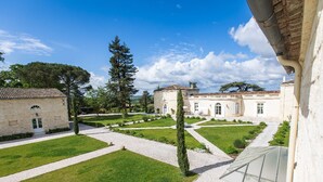 A courtyard with a stone building, a large tree, and a well-maintained lawn. - Château Gassies Gîte "Calèche" (LATRESNE)