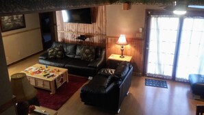 A cozy living room with a black leather sofa, a wooden coffee table, and a lamp on a side table. - Remodeled Vacation Home in the Mountains - Upstairs Balconies, Patios &... (Corryton)