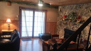 A cozy living room with a stone wall, a fireplace, a dining table with chairs, a leather sofa, and a lamp. - Remodeled Vacation Home in the Mountains - Upstairs Balconies, Patios &... (Corryton)