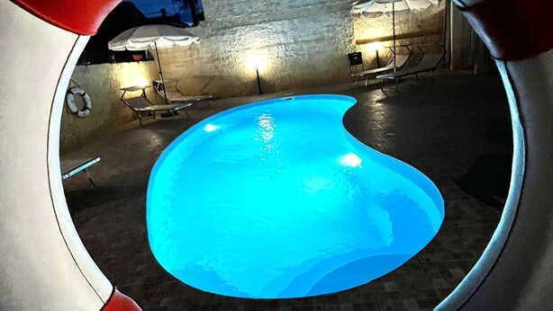 Une piscine circulaire, dont l’intérieur est de couleur bleue, entourée d’un petit muret et d’une rambarde rouge.