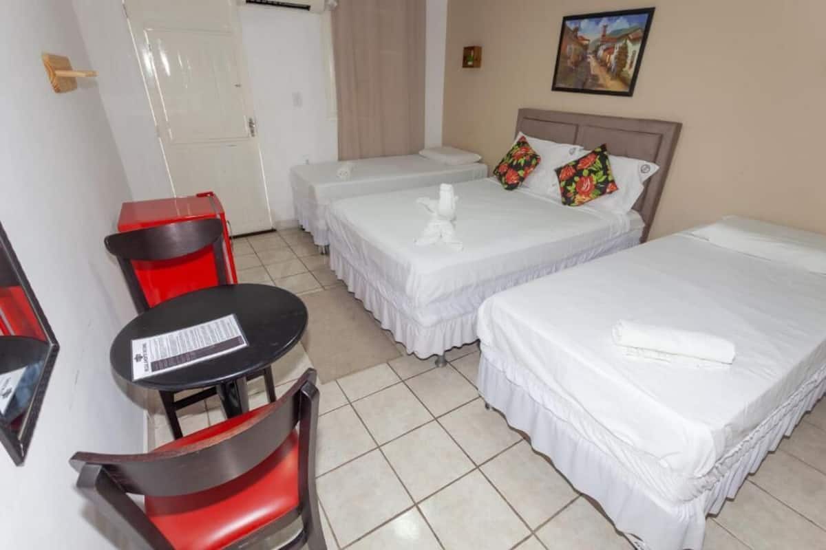 Quarto de hotel com duas camas de solteiro, uma mesa pequena com uma cadeira e uma porta.
