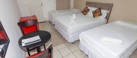 A hotel room with two single beds, a small table with a chair, and a door.