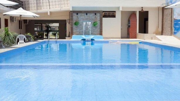 Ein Schwimmbecken mit einer Springbrunnenanlage, umgeben von Liegestühlen und Sonnenschirmen.