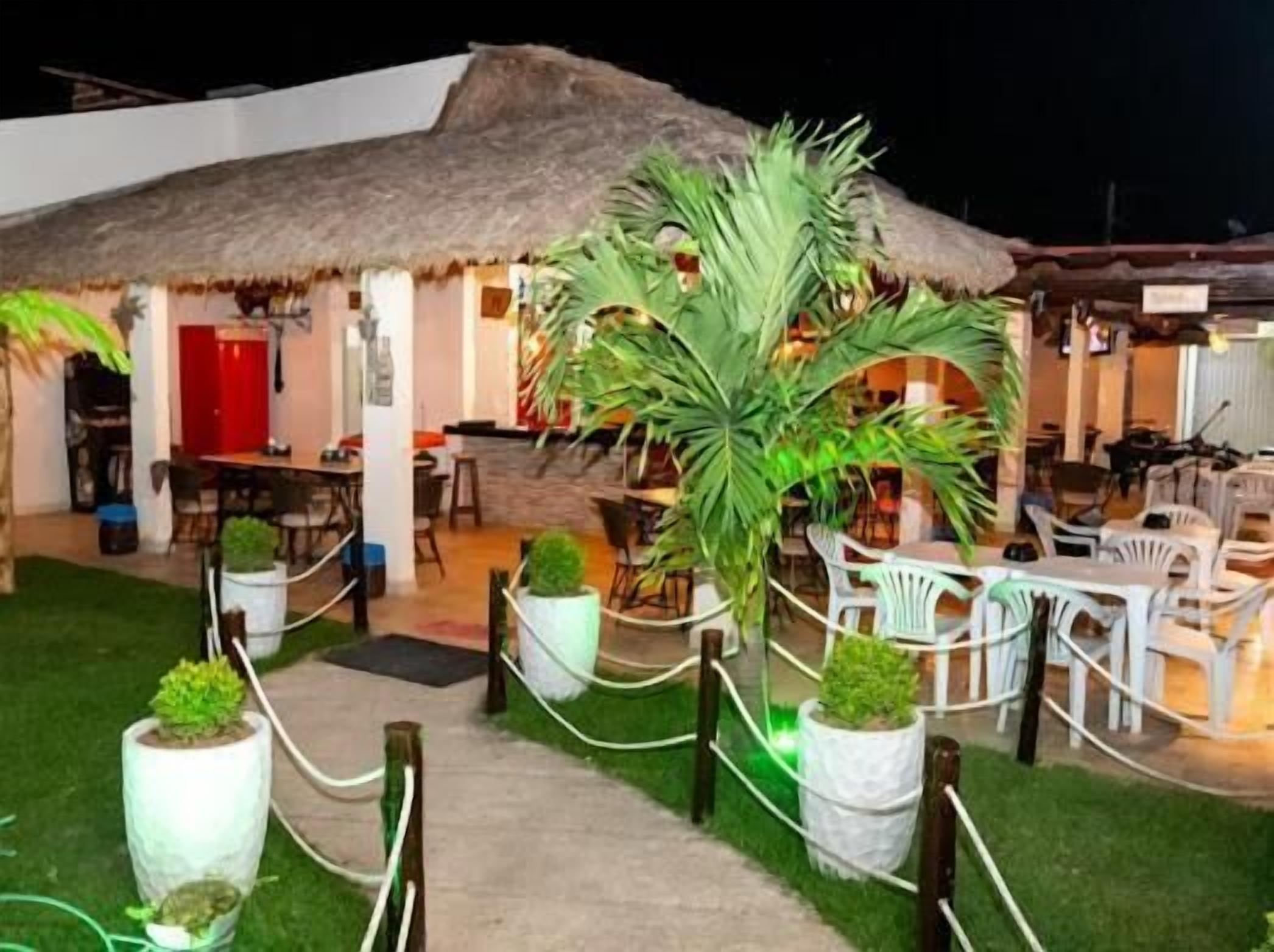 A thatched-roof structure with outdoor seating, surrounded by potted plants and a pathway.