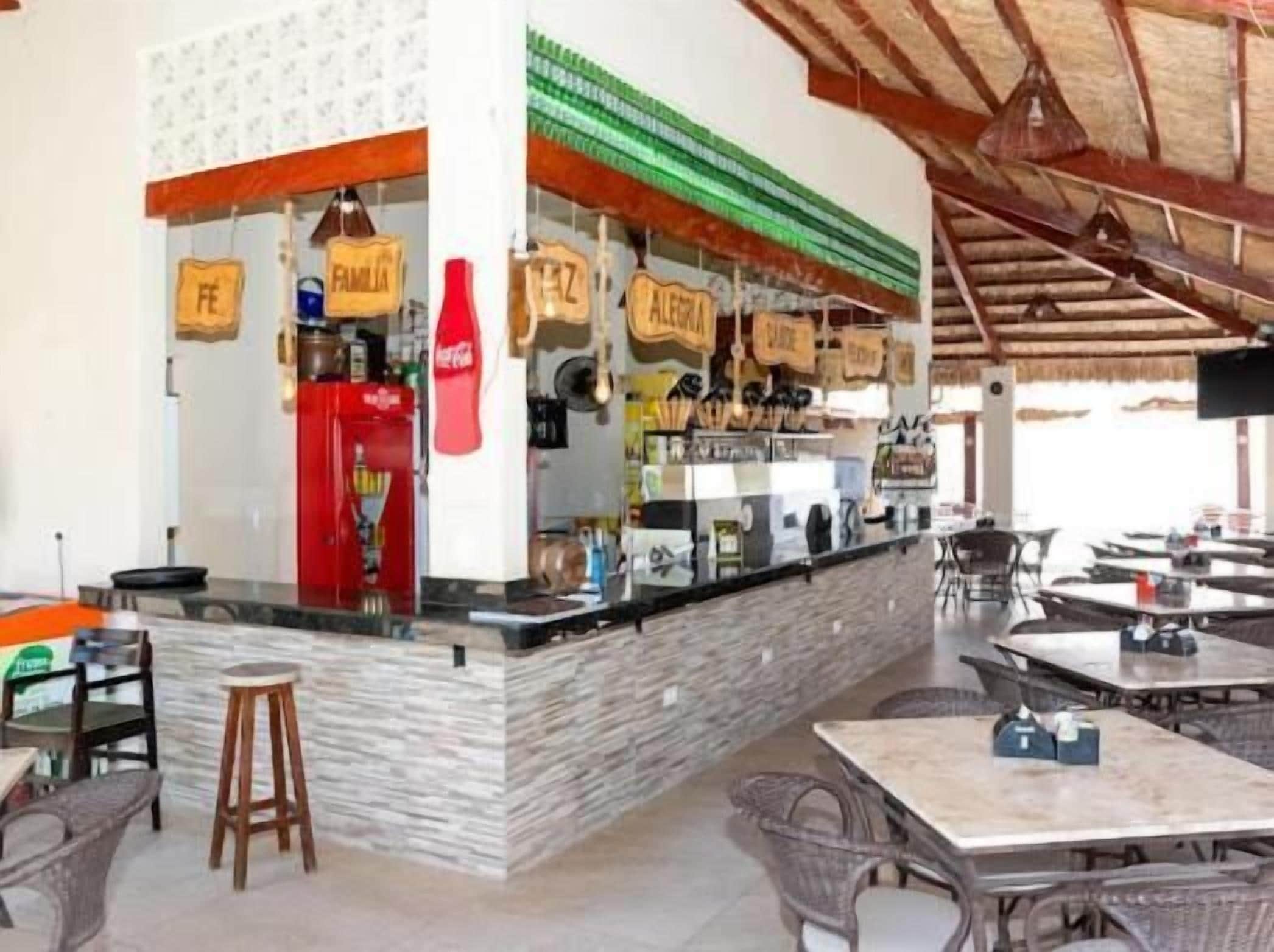 Un café al aire libre con mostrador, zona de estar y techo de paja.