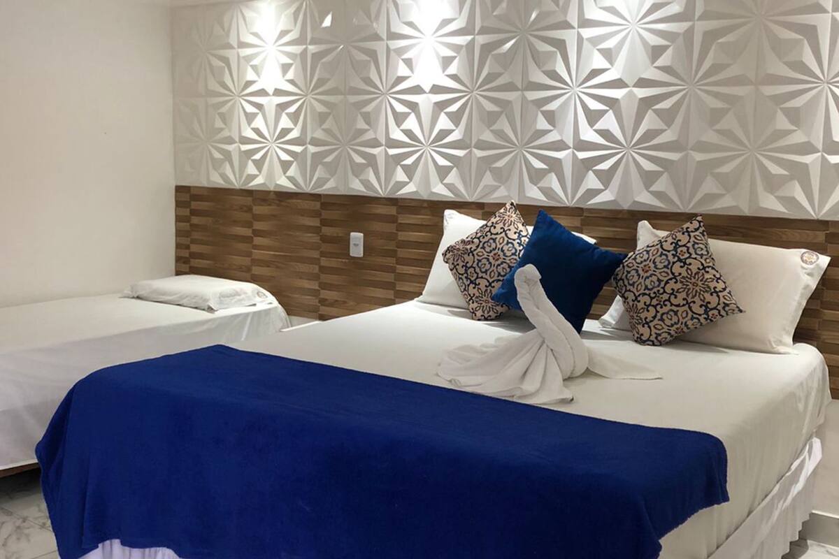 Quarto de hotel com duas camas, um painel decorativo e um cobreleito azul.